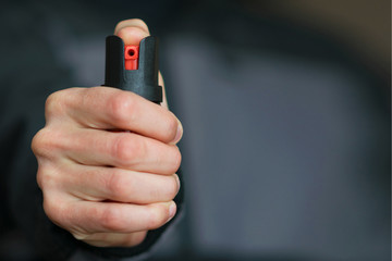 Man holding pepper spray (tear gas) in his hand. Self-defense. Blur background, close up.