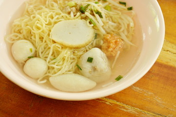 Chinese egg noodles topping fish dumpling and shrimp ball in clear soup on bowl