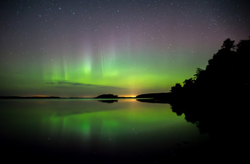 Obraz na płótnie Canvas Northern lights dancing over calm lake in Farnebofjarden national park in Sweden.