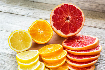 Sliced fresh lemons, grapefruits, oranges on a wooden cutting board with a knife