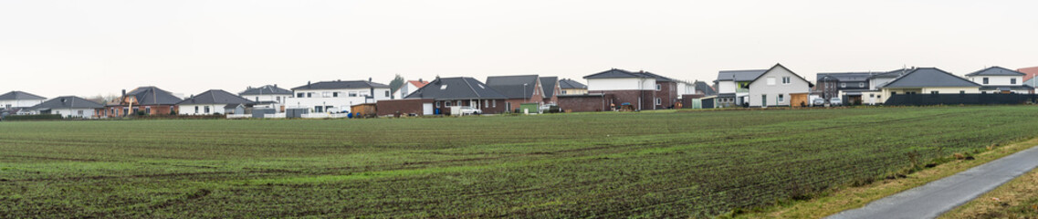 Fototapeta na wymiar Panorama of a new housing estate with single-family houses on the edge of a village with arable land, lots of space and width as a header for a website
