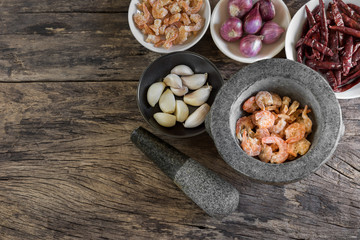 top view of raw dried shrimp in stone mortar with spices ingredient for thai food prepare to crushed on old and crack wooden board, copy space for text. healthy food concept.