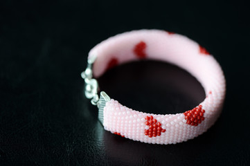 Pink beaded bracelet with images of red hearts on a dark background close up