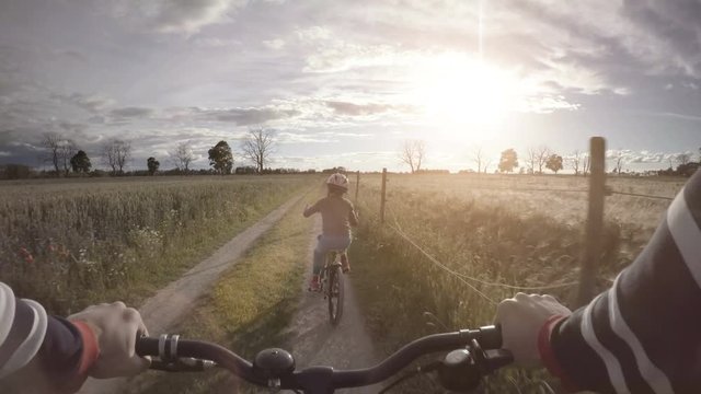 Little girl riding bicycle on rural road. Summer lifestyle moment of a happy childhood.