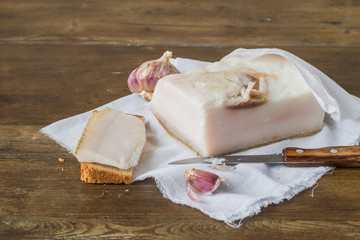 A piece of salted lard and black rye bread on a white cotton napkin on an old wooden table. 