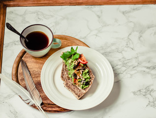 Toast of gluten fries with guacamole with tomatoes, seeds and herbs. A cup of coffee. Breakfast. Wooden board.Marble background. Top view.