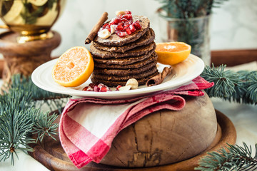 Chocolate banana pancakes with pomegranate and mandarin, winter vegan breakfast..New Year Christmas background.