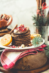 Obraz na płótnie Canvas Chocolate banana pancakes with pomegranate and mandarin, winter vegan breakfast..New Year Christmas background. Selective focus.