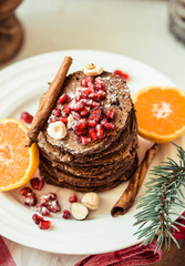 Chocolate banana pancakes with pomegranate and mandarin, winter vegan breakfast..Close-up.