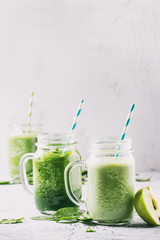 Variety of three color green spinach kale apple yogurt smoothie in mason jars with retro cocktail tubes over gray background. Healthy vegan detox eating. Toned image