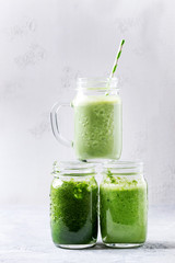 Variety of three color green spinach kale apple yogurt smoothie in mason jars on each other over gray background. Healthy vegan detox eating.