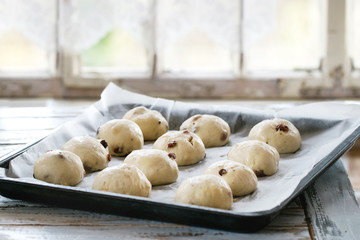 Raw unbaked buns. Ready to bake homemade Easter traditional hot cross buns on oven tray with baking paper over white wooden table with window at background. Natural day light. Rustic style.