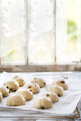 Raw unbaked buns. Ready to bake homemade Easter traditional hot cross buns on baking paper over white wooden table with window at background. Natural day light. Rustic style.