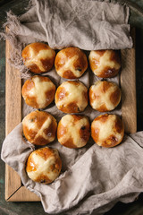 Homemade Easter traditional hot cross buns on wooden tray with textile over old dark metal background. Top view, space