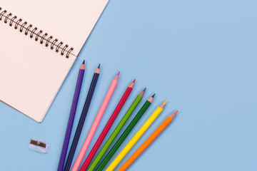 top view of blank notebook coloured pencils and shrappener on light blue background with copy space. memo and planning concept.