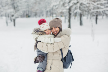 Fototapeta na wymiar Brunette young women portrait with baby girl, daughter hugs and smiling in snowy park.