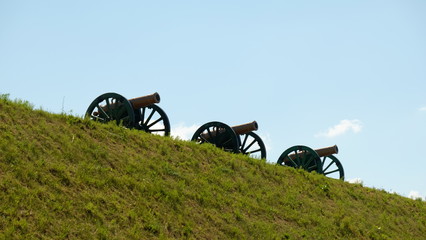 Three old guns on a green grass slope against the background of a clean sky.