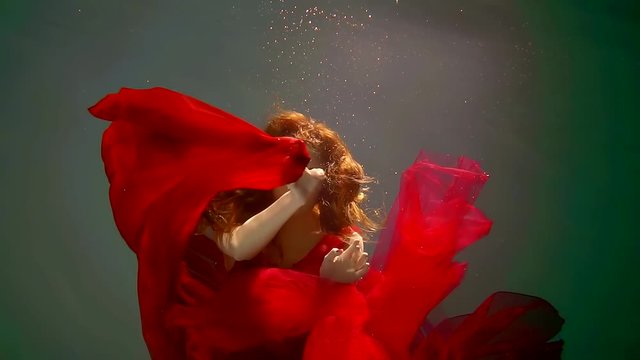 Seductive young woman is hiding behind her amazing red dress deep underwater.