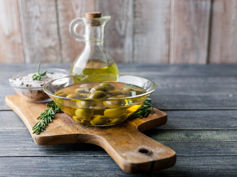 Olive oil in countess and olives with spices and fragrant herbs on a wooden background.