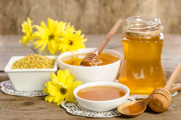 Yellow flowers and bee products (honey, pollen) on wooden background