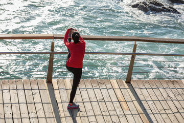 sporty fitness female warming up stretching legs on seaside boardwalk