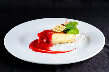 Delicious cheesecake with jam, citrus, mint and powdered sugar on the plate on dark background