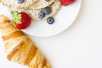Healthy Breakfast Concept: a french croissant and breadcrisps with fresh strawberries and blueberries on white, top view, copy space
