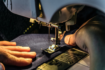 Seamstress work on the sewing machine. Night work by the light of the built-in hardware lamp. Machine sewing needle with looper and presser foot close-up.