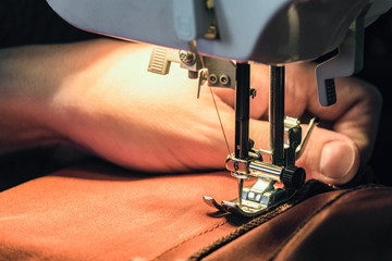 Seamstress sews clothes made of red cloth on a sewing machine. Work by the light of the built-in...
