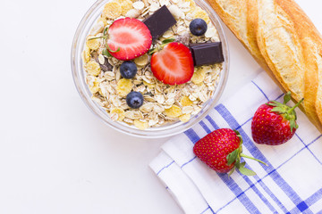 Healthy Delicious Breakfast Concept with a bowl of cereal with fresh berries and chocolate and french baguette, top view. White background with a napkin