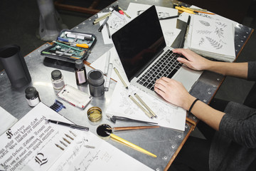 The artist's hand behind the laptop. The hands of a master calligrapher. Tattoo artist the artist makes a sketch, sitting at a table in the Studio top view