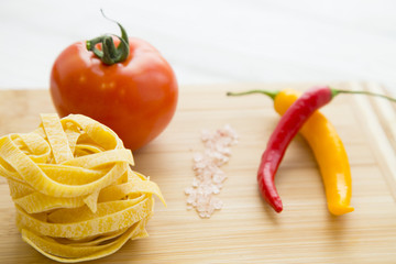 Preparing Food Concept. Ingredients for italian pasta with red and yellow cayenne chilli peppers and tomatos on a wooden cutting board, close up