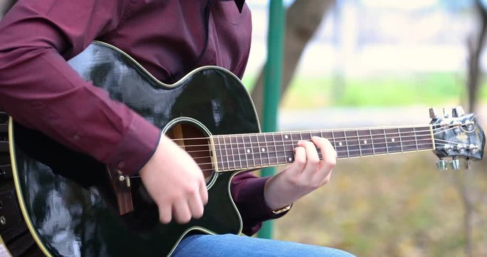 Young man playing acoustic guitar outdoors closeup