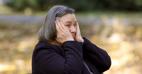 Depressed senior woman thinking worried outdoors in park.