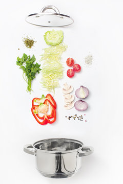 Assorted fresh vegetables falling into a bowl, on white background