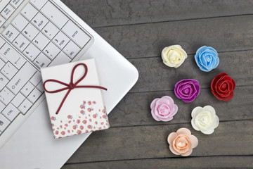 Laptop, gift box and seven roses on wooden board