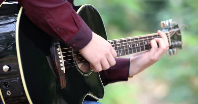 Young man playing acoustic guitar artist musician outdoors