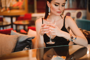 A beautiful girl drinks martini in the hotel lobby and is waiting for her young boyfriend