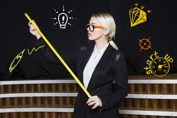 Beauty blonde businesswoman with designer or architect staff is standing against concrete wall with startup sketch on it
