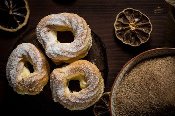 Three sweet cream puffs on dark board with cinnamon sugar in bowl