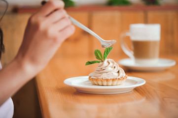 Woman eating a cake of cottage cheese in a ceramic plate with a spoon on a wooden table