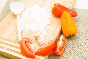 Kitchen, Baking, Pastry Concept. A wooden cutting board with a heap of flour and a wooden spoon, sliced tomato and peppers on a linen cloth