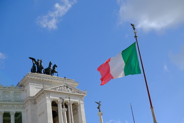 Italian flag waving against the statue of the goddess Victoria riding on quadriga on the top of the Altar of the Fatherland from Piazza Venezia, Rome, Italy