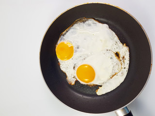Fried eggs in pan with isolated white background, top view.