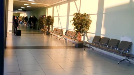 Back view of passenger walking and carrying a suit case in an airport