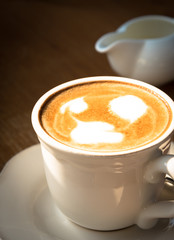 A cup of coffee with valentine milk foam on the white plate and wooden table.