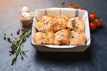 Fresh chicken hips marinated in a bowl with cooking ingredients on black background.