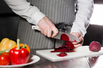 Obraz na płótnie Canvas Young chef cutting beet on a white cutting board. Closeup of hand with knife cutting fresh vegetable. Cooking in a restaurant kitchen