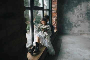 Obraz na płótnie Canvas Cheerful bride with bouquet sits on the windowsill next to the groom. Artwork