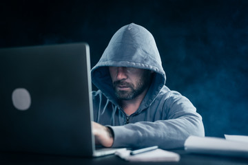 A computer hacker is typing on a laptop in a smoky room. Dark background